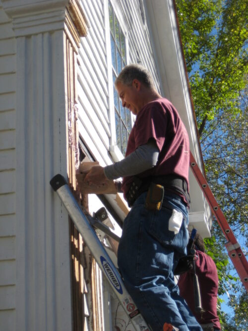 Professional contractor performs exterior home renovation, repairing fluted window trim.
