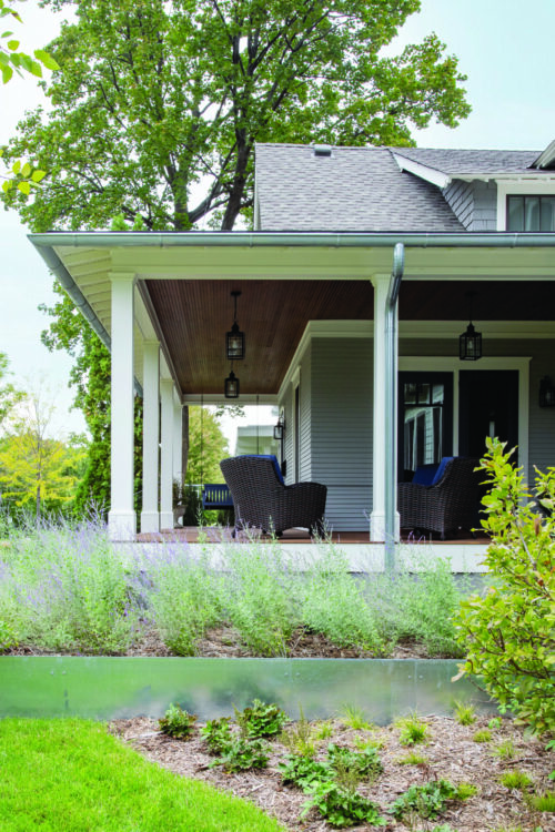 Exterior home renovation features a spacious porch, gray siding, wood ceiling, wicker chairs.