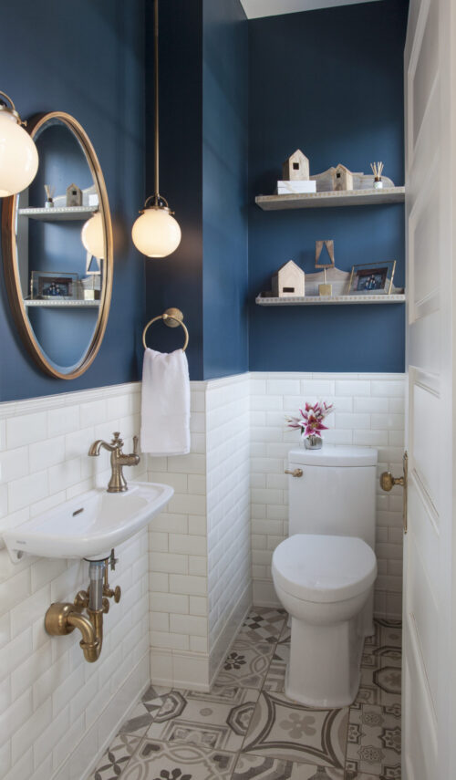 Powder room boasts dark blue walls, white subway tile, and patterned floor. Brass fixtures and globe pendants complete bathroom remodel. Twin Cities.