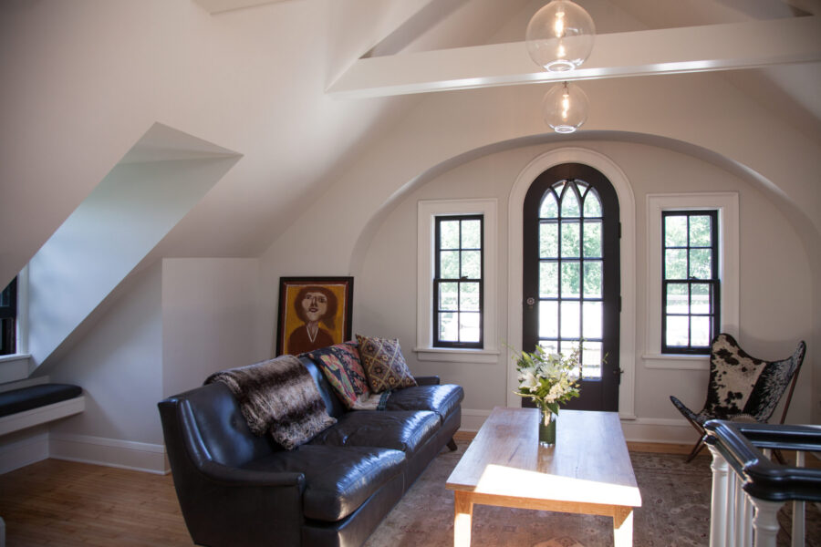 Twin Cities attic living space renovation features an arched door, exposed beams, window seat, and leather sofa.