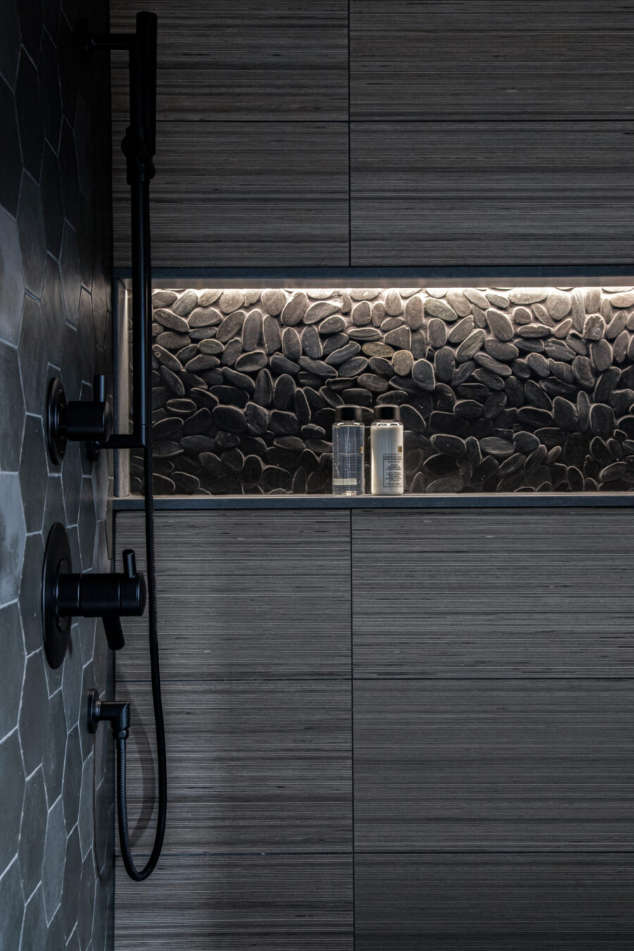 Dark, contemporary Twin Cities bathroom-renovation features hexagonal-tile, illuminated pebble-niche.
