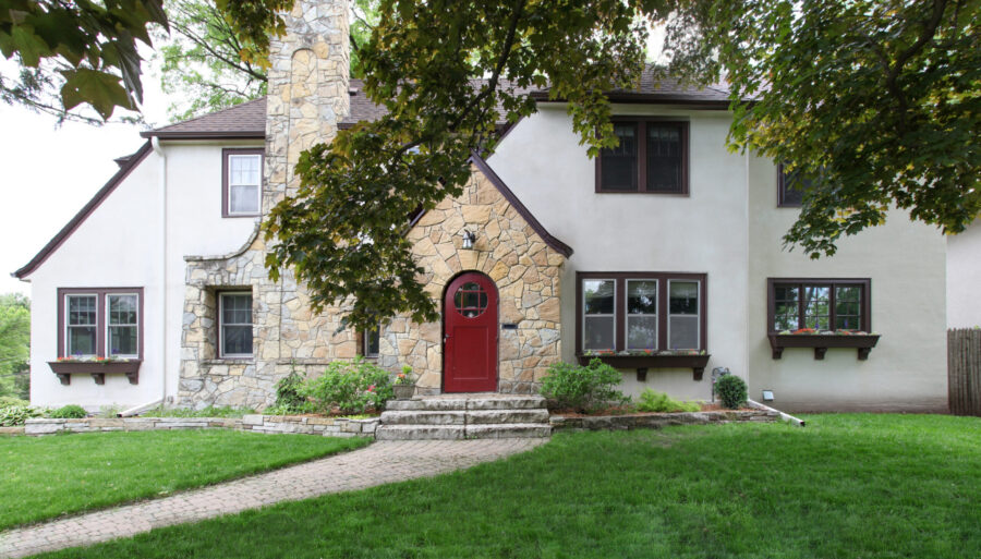 Stucco-and-stone home features a vivid red arched doorway, dark trim.