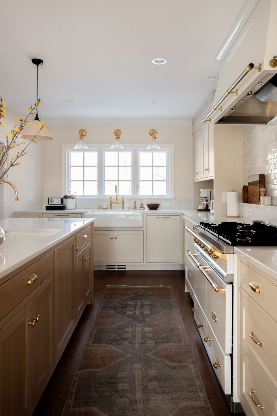 Bright kitchen renovation; cream cabinetry, light island, gold hardware, white farmhouse sink.