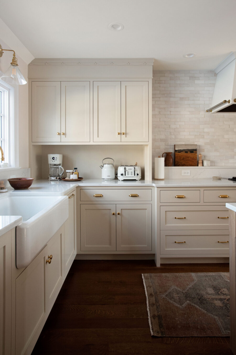 Neutral kitchen remodel boasts shaker cabinets, farmhouse sink, and light brick backsplash.