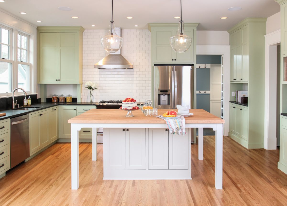 A bright Twin Cities kitchen remodel boasts sage green cabinetry, white subway tile, light wood floors, and a large wood island.