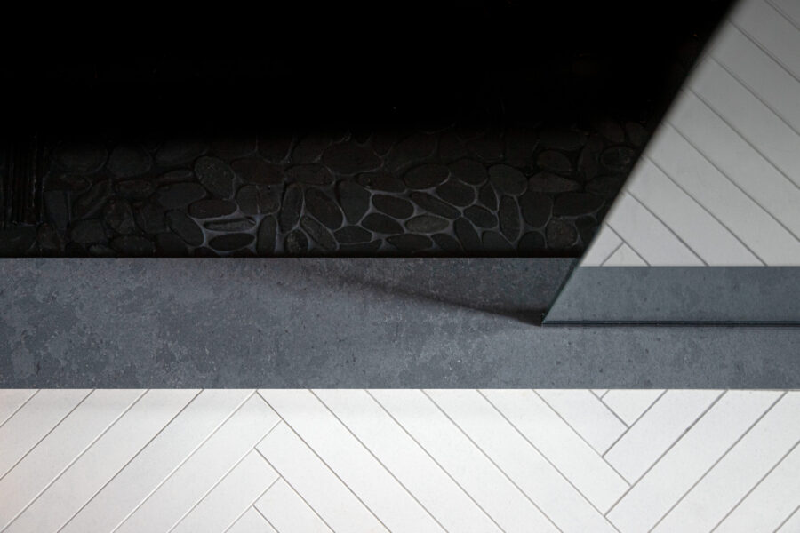 Modern bathroom remodel features dark pebble floor, grey concrete slab, and white herringbone tiles, a Twin Cities design build.