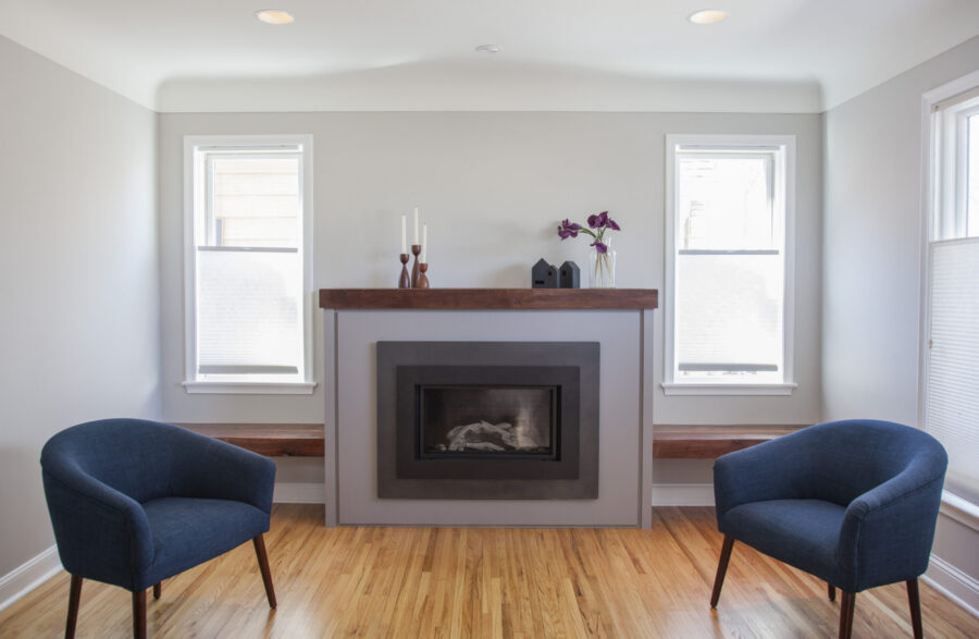 Renovated Twin Cities living room displays modern fireplace, wood flooring, and blue armchairs.