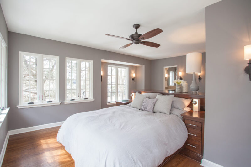 Twin Cities bedroom renovation features serene gray walls, hardwood flooring, and a custom dark wood headboard with integrated lighting.
