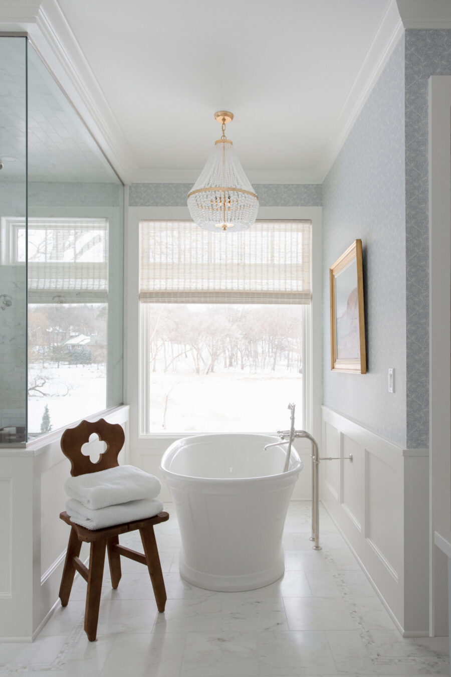 Twin Cities bathroom renovation features freestanding tub, marble floor, wainscoting, and chandelier.