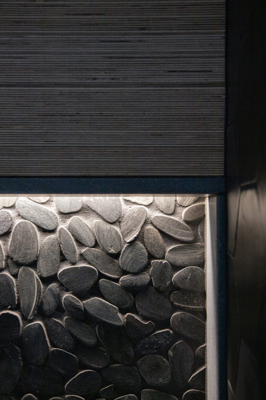 Illuminated pebble wall accentuates dark grooved paneling. Twin Cities bathroom remodel design.