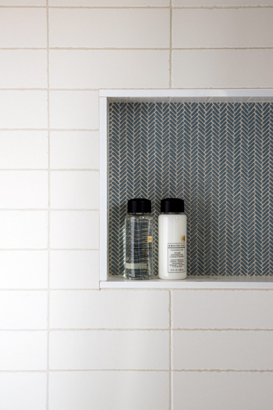 Twin Cities home renovation installs a white-tiled herringbone shower niche.