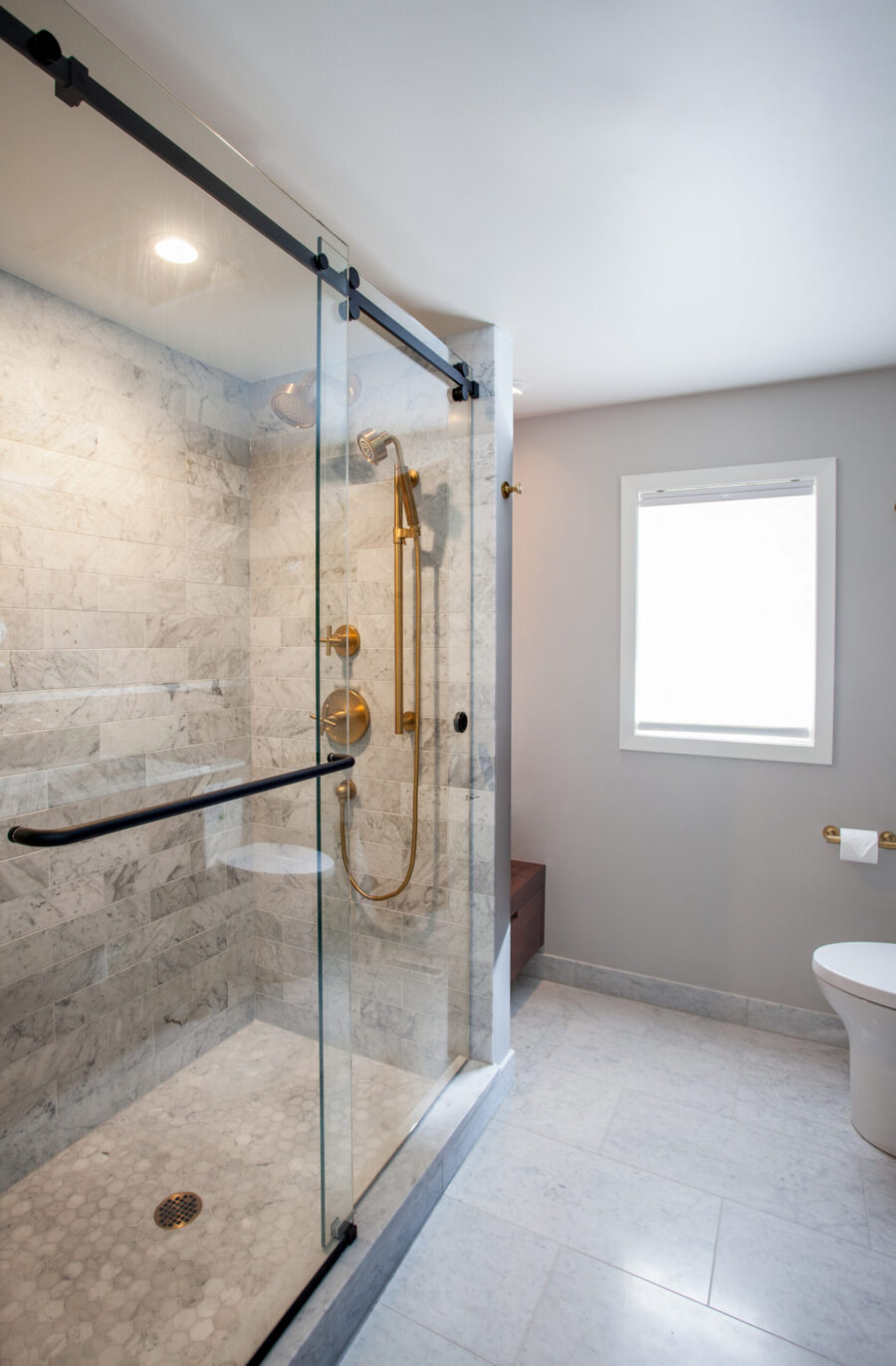 Twin Cities bathroom remodel: bright marble shower, hexagonal shower floor, brass fixtures.