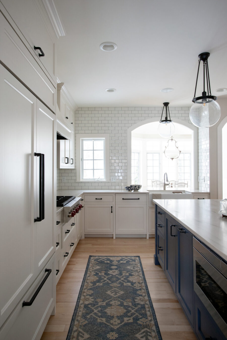 Contemporary white kitchen remodel features cabinetry, large island, and subway tiling.