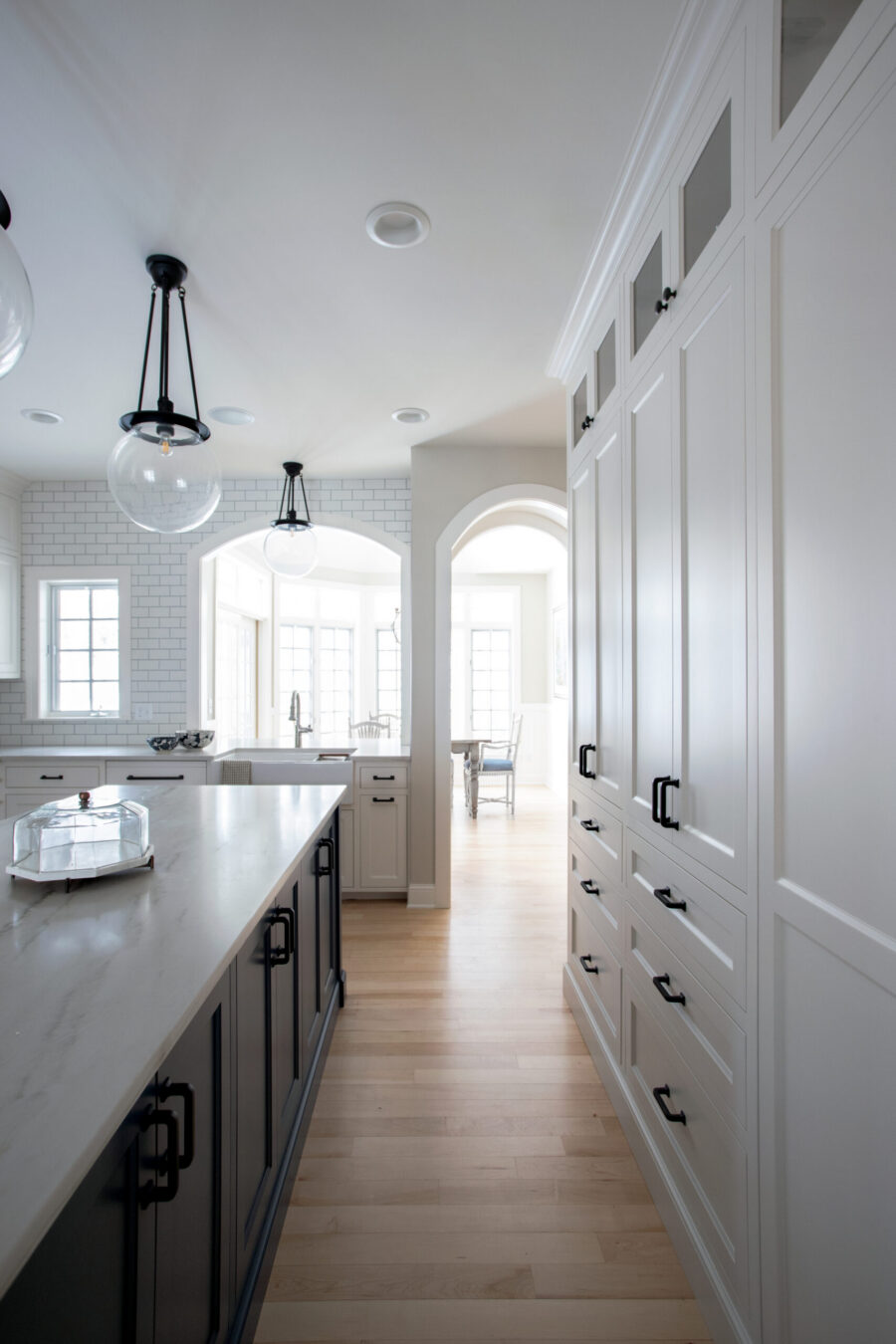 Twin Cities kitchen remodel features white cabinets, dark island, marble counters, and wood floors. Globe pendants illuminate.
