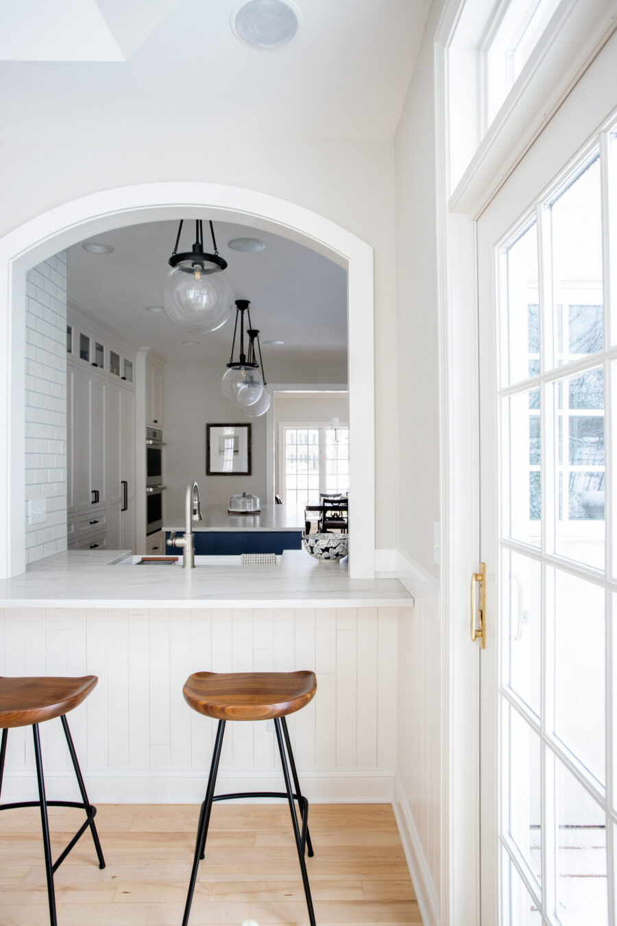 A Twin Cities kitchen remodel. Arched opening, marble counter, wood stools, and globe pendant lights define the bright space.