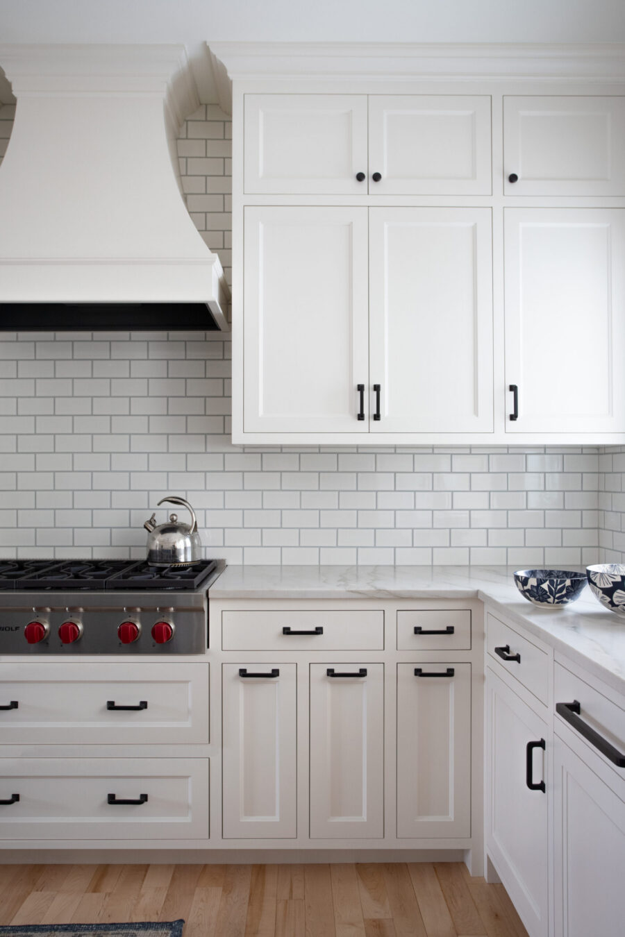 White kitchen remodel offers shaker cabinets, black hardware, subway tile, marble, gas range, wood floor.