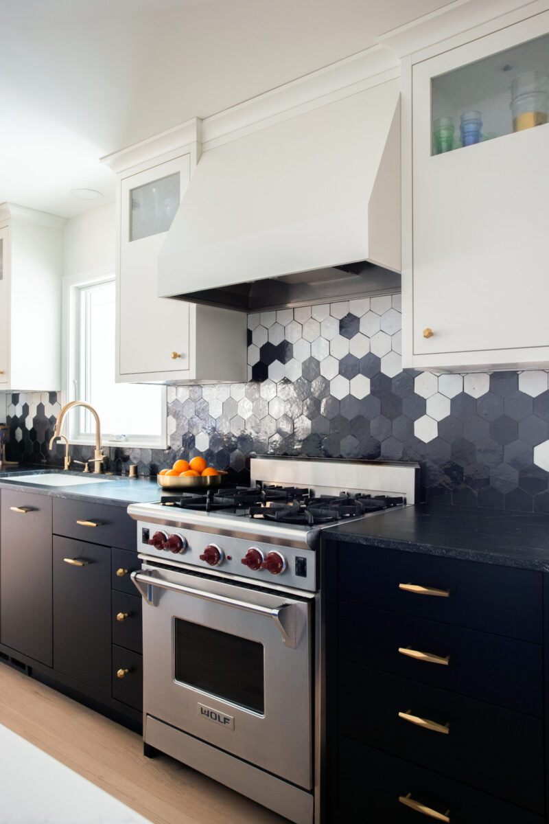 Twin Cities kitchen remodel features white and dark cabinetry, hexagonal backsplash, stainless steel range.