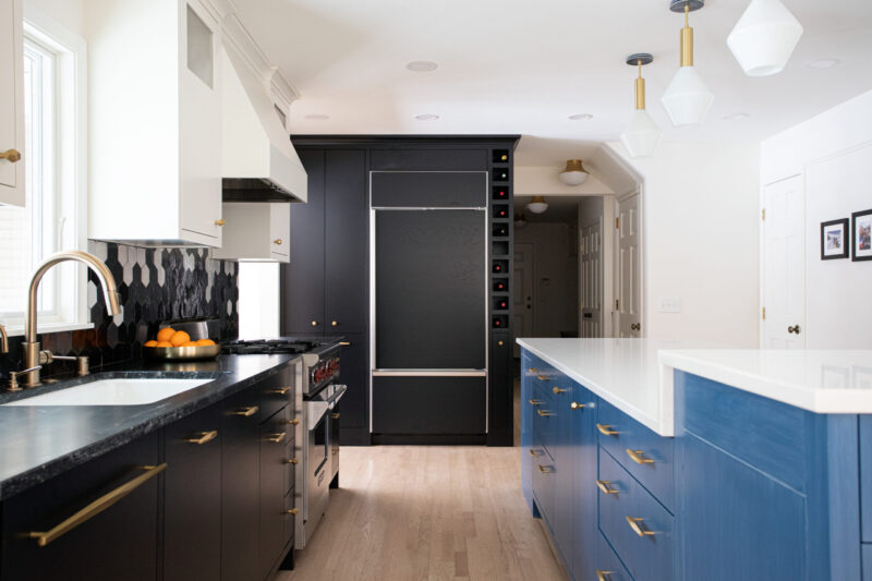 Modern kitchen remodel features black cabinets, a blue island, and hexagonal backsplash. Gold hardware and pendant lighting illuminate the space.