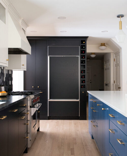 Modern kitchen remodel features black cabinets, a blue island, and hexagonal backsplash. Gold hardware and pendant lighting illuminate the space.
