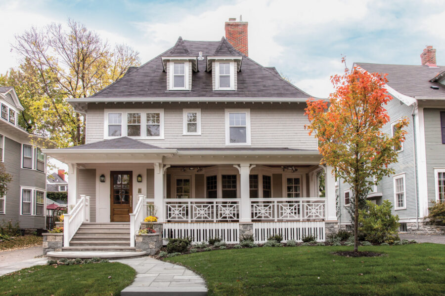Updated exterior: light-shingled residence. Broad, white, stone-based porch. Dark-roofed. Autumn tree.