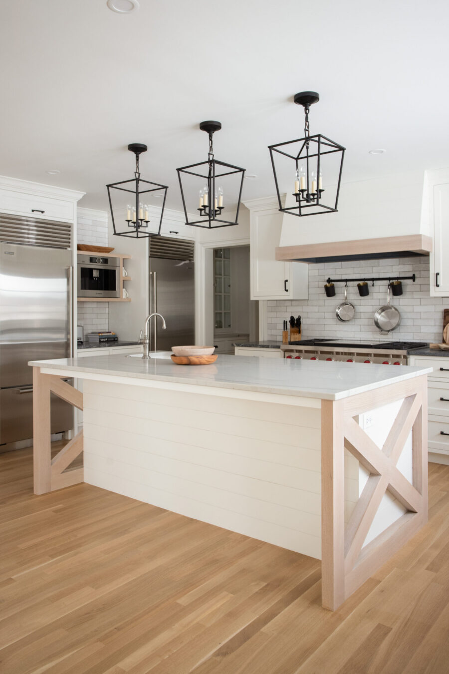 Expansive bright kitchen renovation: white cabinetry, light wood flooring, large island pendants.