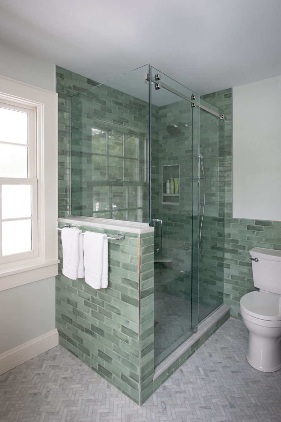 Twin Cities bathroom remodel features a walk-in glass shower, green subway tile, and herringbone marble floor.