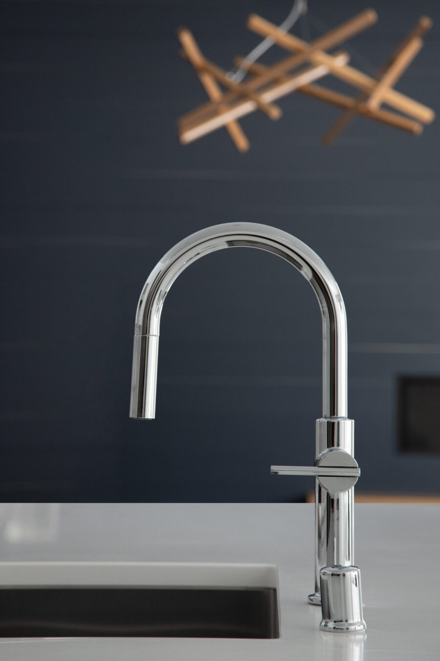 Polished chrome kitchen faucet elevates a white countertop in a modern Twin Cities kitchen remodel. A wood chandelier blurs above.