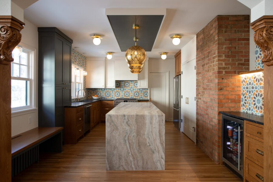 Twin Cities kitchen remodel features a veined stone island, brass pendant lights, patterned tile, mixed cabinetry, exposed brick.