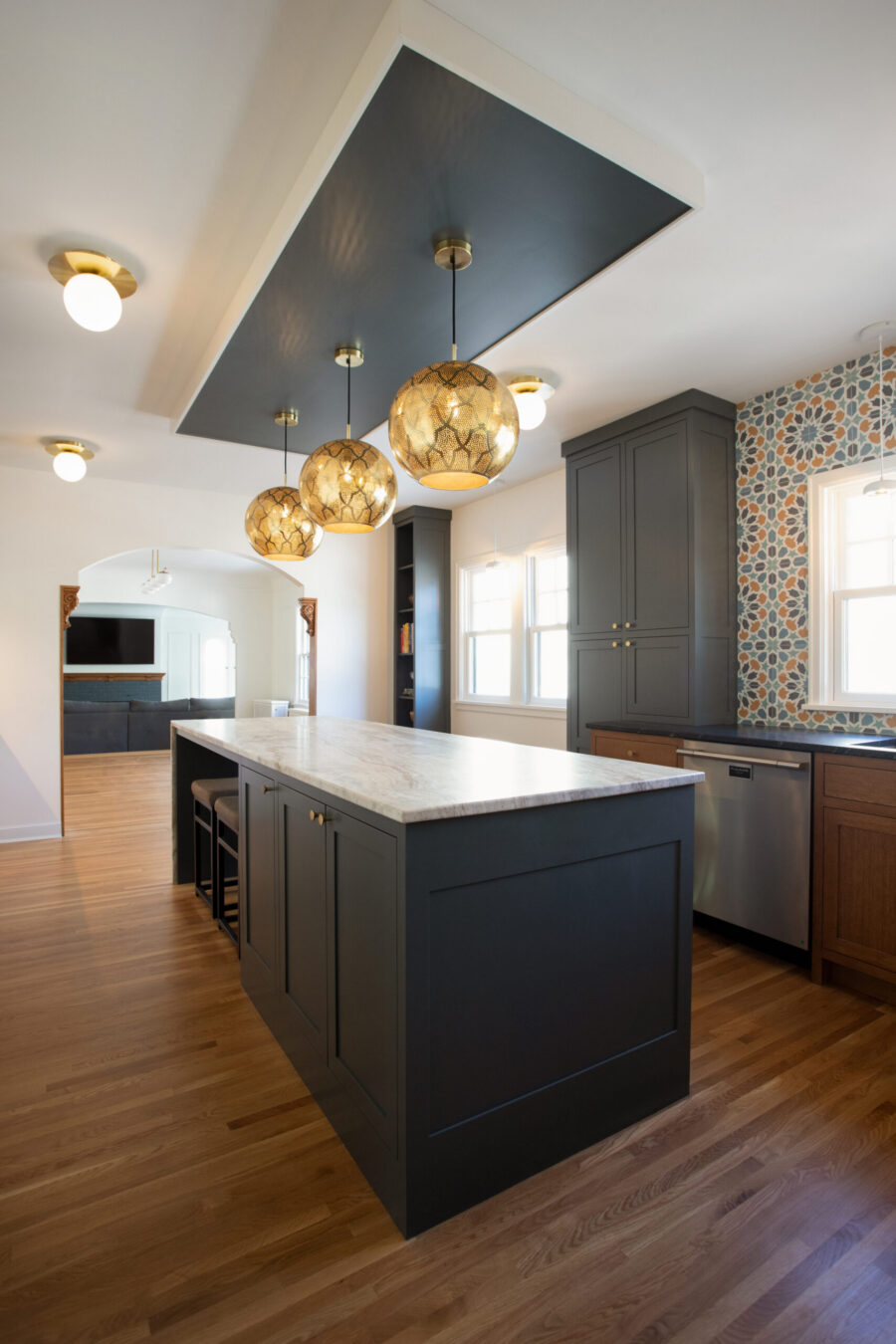 Kitchen remodel: dark island, light marble counter, brass pendants, geometric patterned tile.