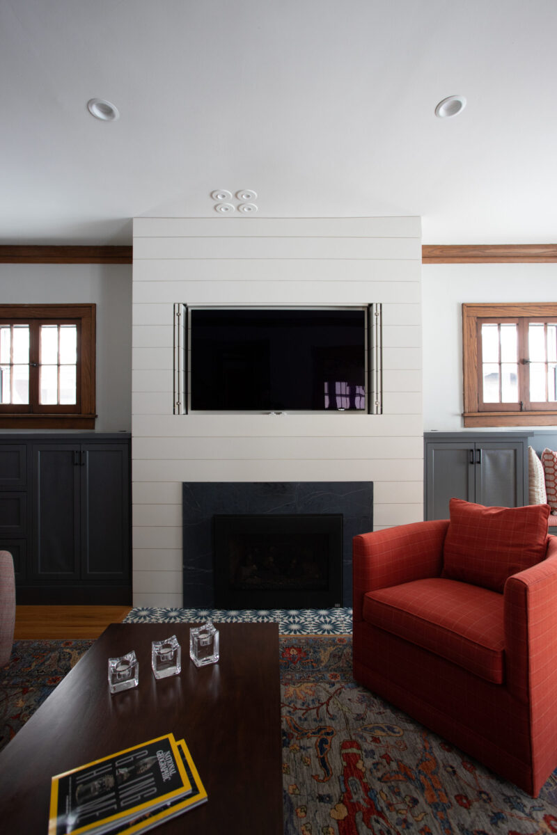 Living room renovation includes shiplap fireplace, dark cabinetry, TV, armchair.