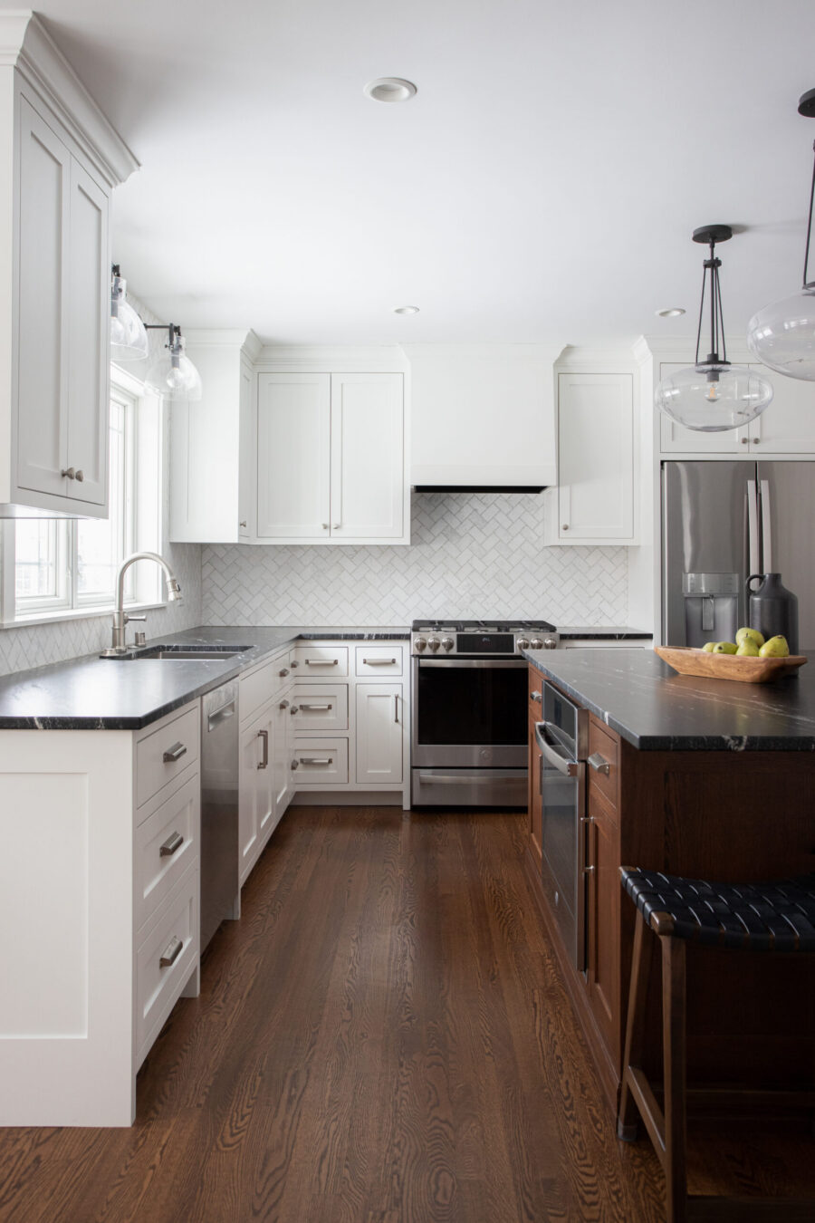Bright Twin Cities kitchen remodel features white shaker cabinets, dark countertops, herringbone backsplash, wood floors.
