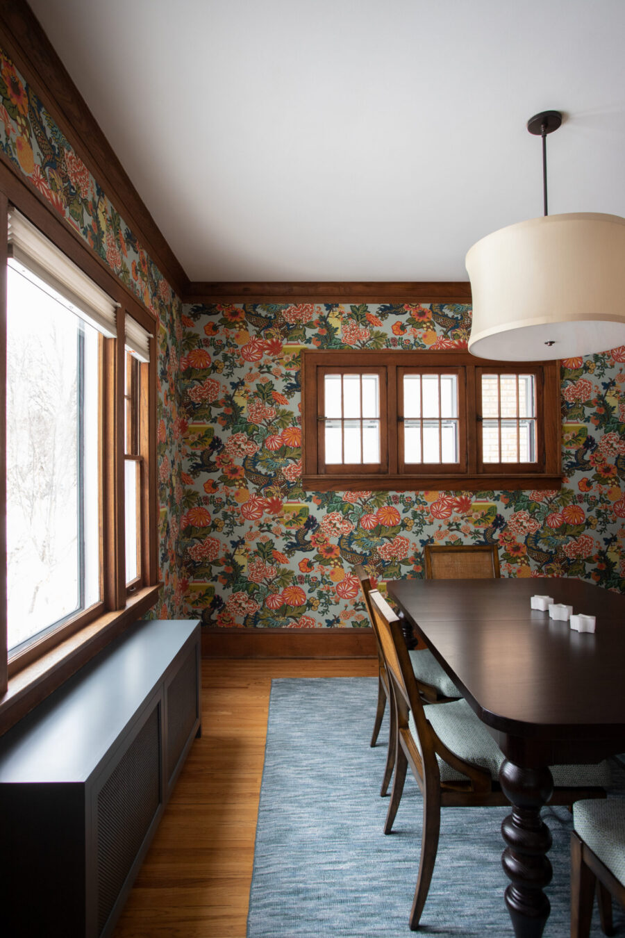 Twin Cities dining room renovation: bold floral wallpaper, dark wood trim, pendant light, wood floor, blue rug.