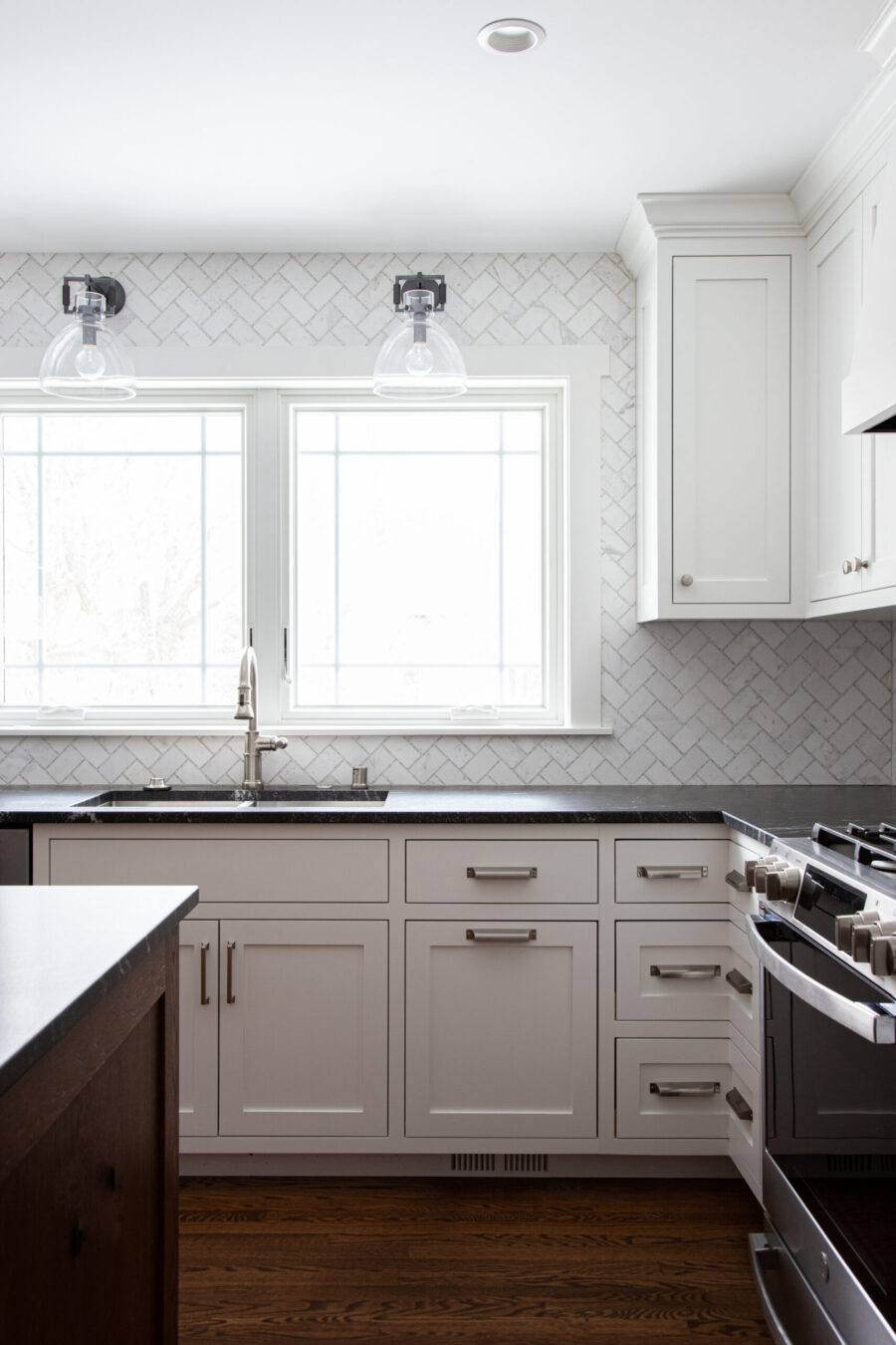 This bright Twin Cities kitchen remodel features white shaker cabinets, dark countertops, a herringbone tile backsplash, and wood floors.
