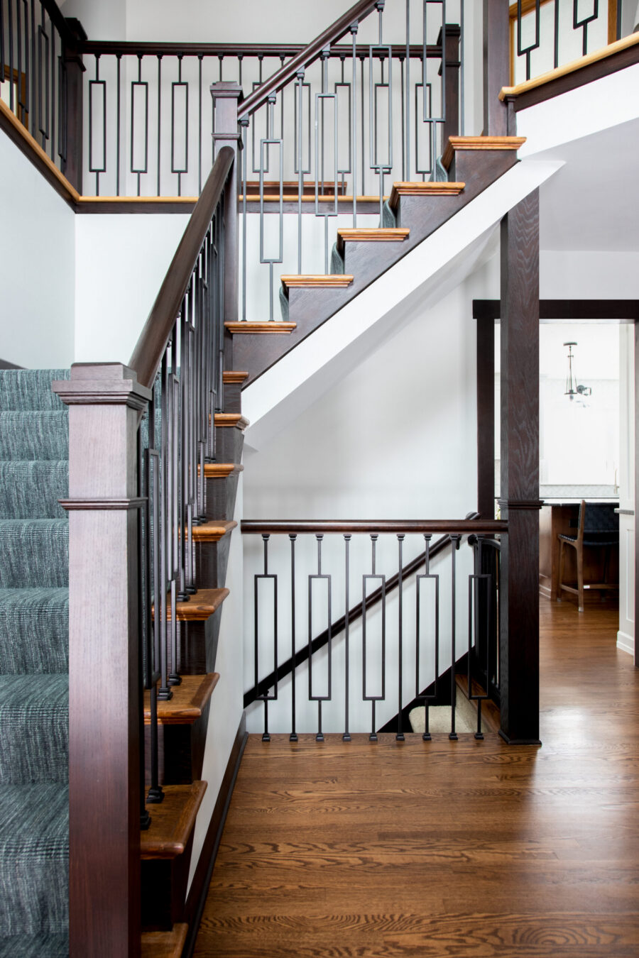 Dark wood staircase, geometric metal balusters, carpet, hardwood defines renovation.