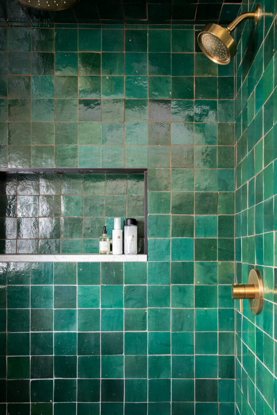 Emerald-green zellige-tiled shower features bright brass fixtures, marble-recessed niche.