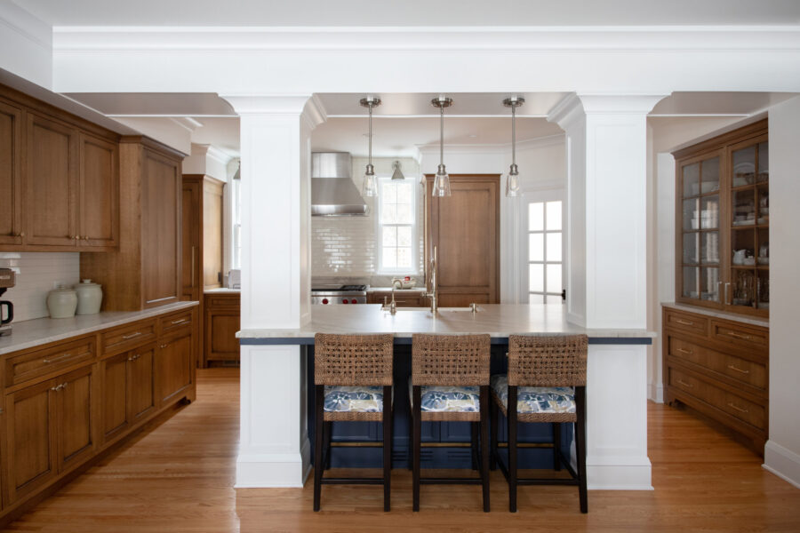Kitchen remodel features warm oak cabinetry, dark-blue island, architectural columns.