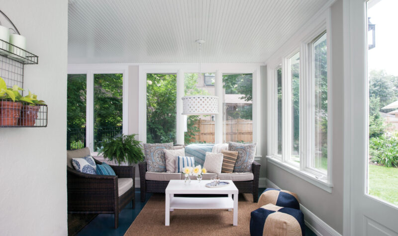 Bright sunroom renovation features white beadboard ceiling, tall windows, wicker furniture.