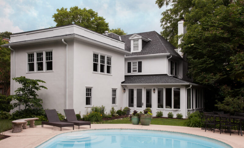 White stucco architectural remodel: dark-roofed, inground-pool-equipped, patio, lush gardens.