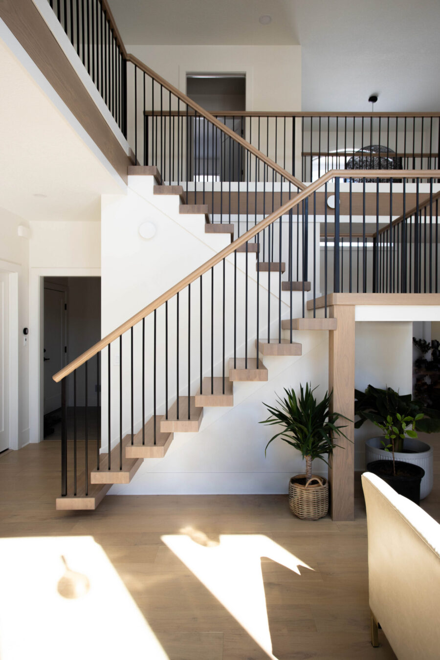 Twin Cities home renovation boasts floating light-wood staircase, black balusters, sunlit wood floors.