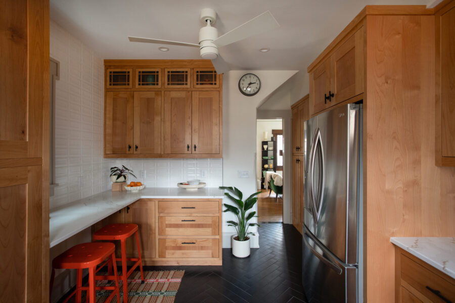 Twin Cities kitchen remodel unveils warm-toned cabinetry, gleaming white counters, dark herringbone flooring.