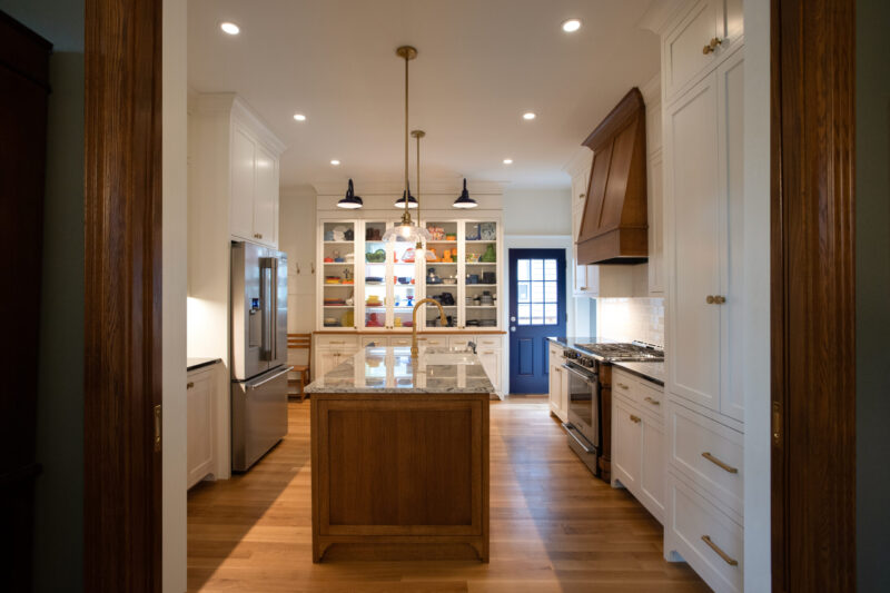 Bright kitchen remodel boasts white cabinets, a wooden island, hardwood floors, a dark wood range hood, and a blue back door.