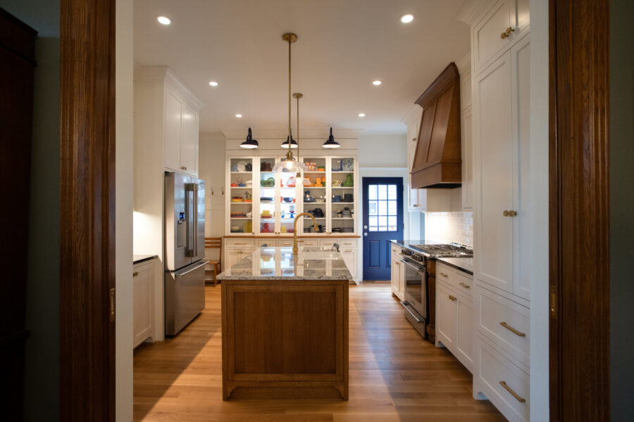 Bright kitchen remodel boasts white cabinets, a wooden island, hardwood floors, a dark wood range hood, and a blue back door.