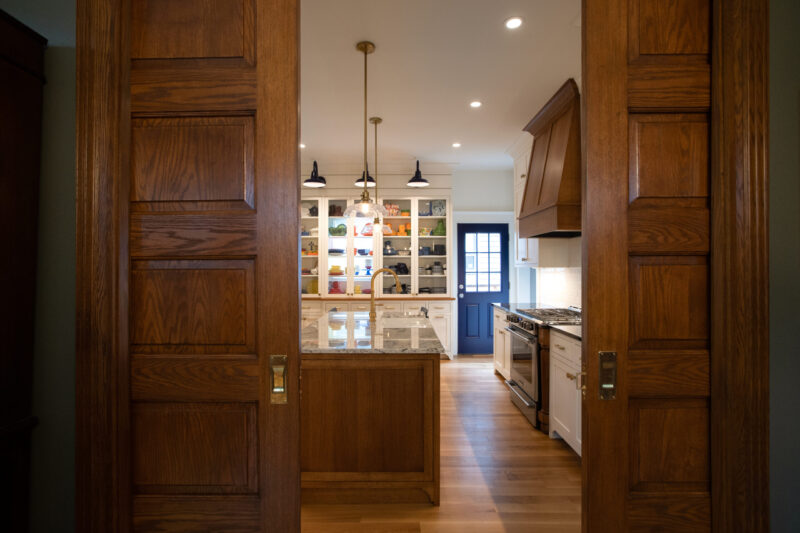 Oak pocket doors frame a bright, renovated Twin Cities kitchen with island, white cabinets, blue door.