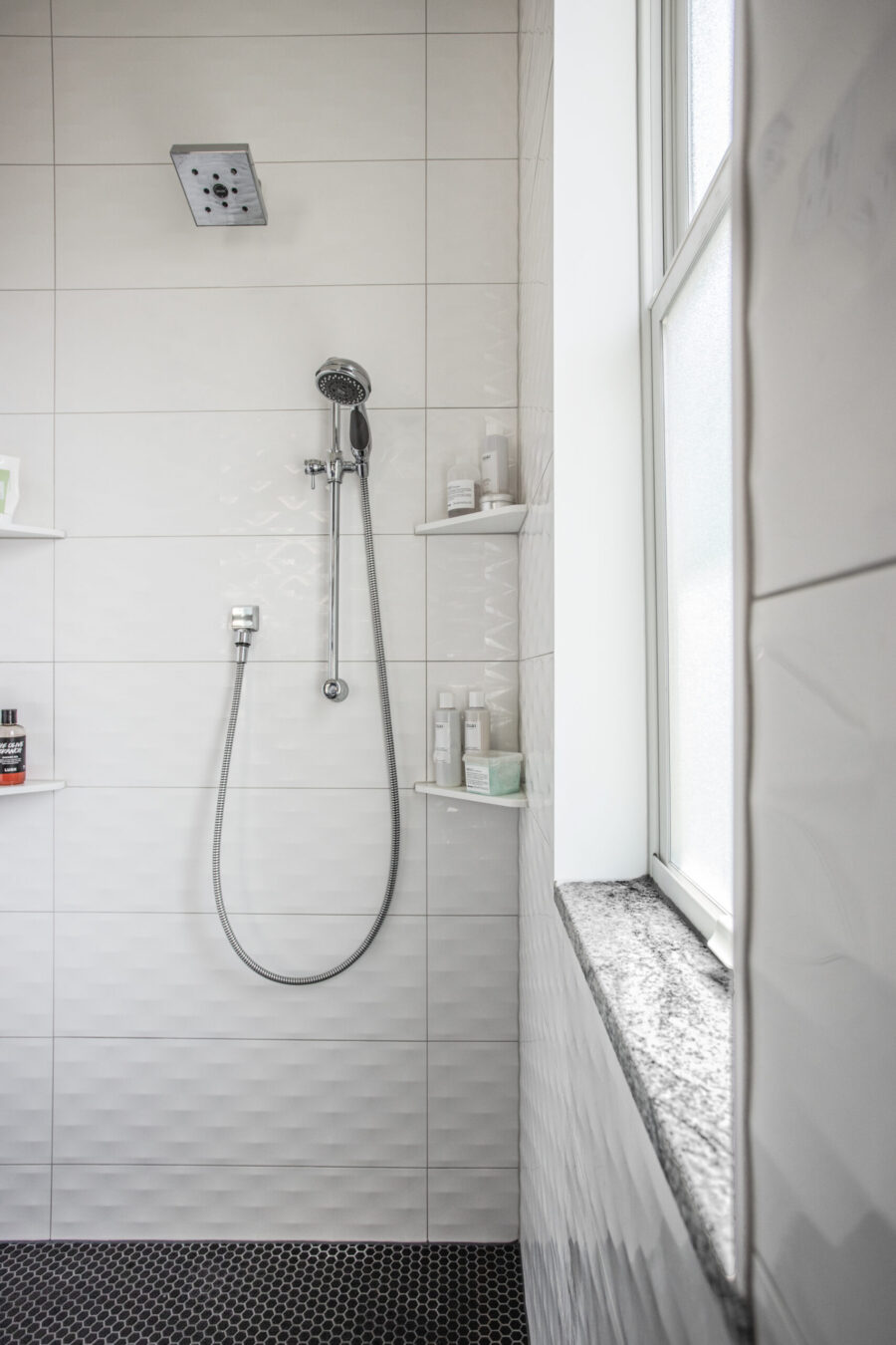 Bright Twin Cities bathroom remodel features white textured tiles, chrome shower, dark hexagon floor, and window.