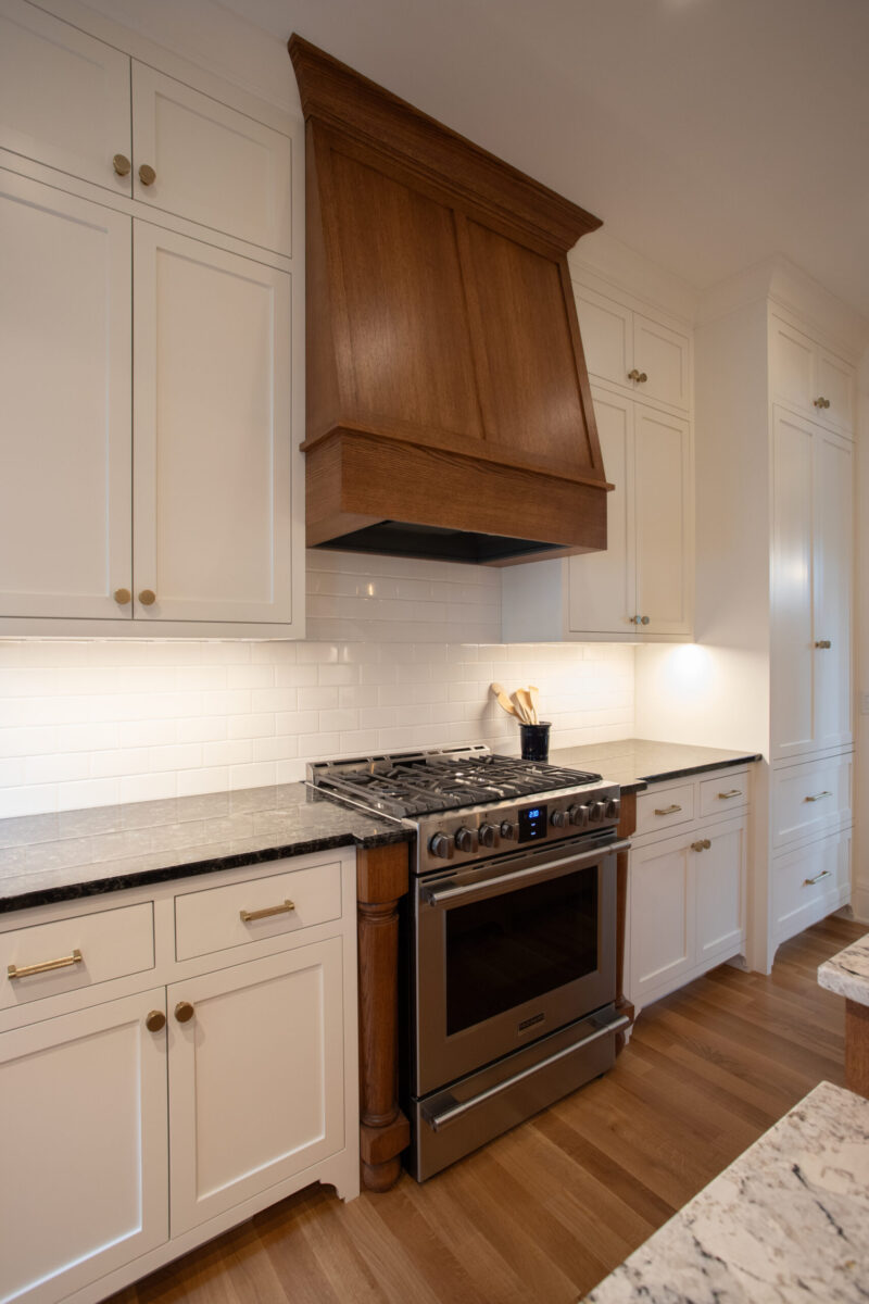 A Twin Cities kitchen remodel features white shaker cabinets, dark granite, custom wood hood, stainless range.