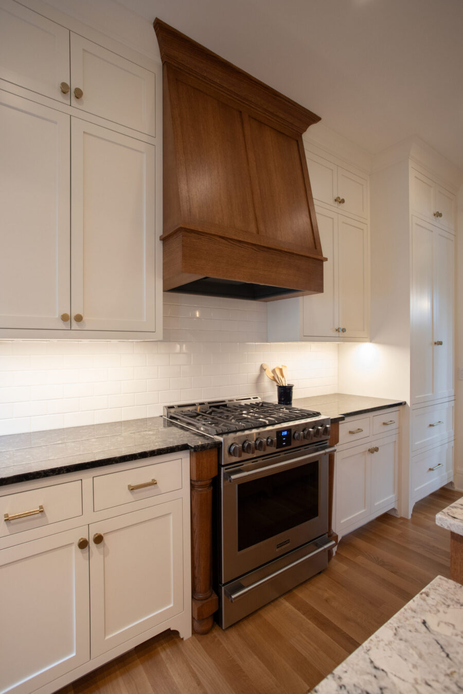 A Twin Cities kitchen remodel features white shaker cabinets, dark granite, custom wood hood, stainless range.