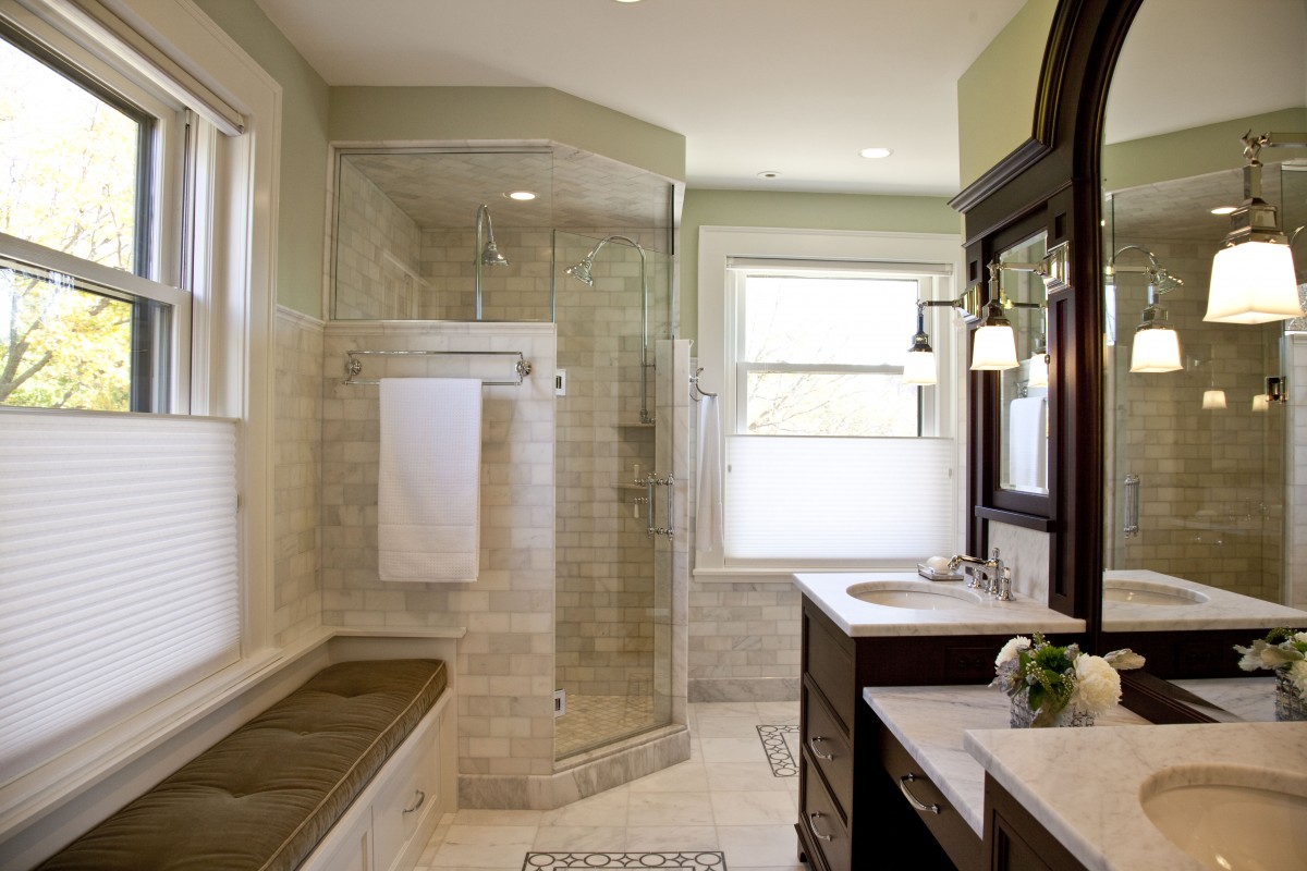 Bathroom renovation provides white marble, glass shower, rich cabinetry, bench.