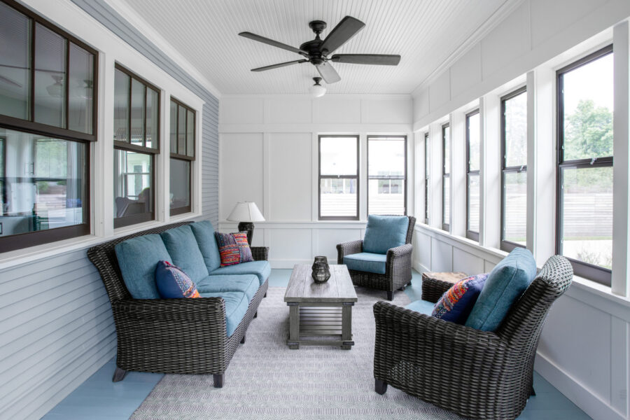 A renovated Twin Cities sunroom features light blue walls, dark-framed windows, a beadboard ceiling, and wicker furniture.