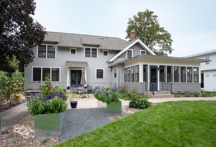 Gray home renovation features screened porch addition and concrete patio with landscaping. Exterior design build uses varying gray siding.