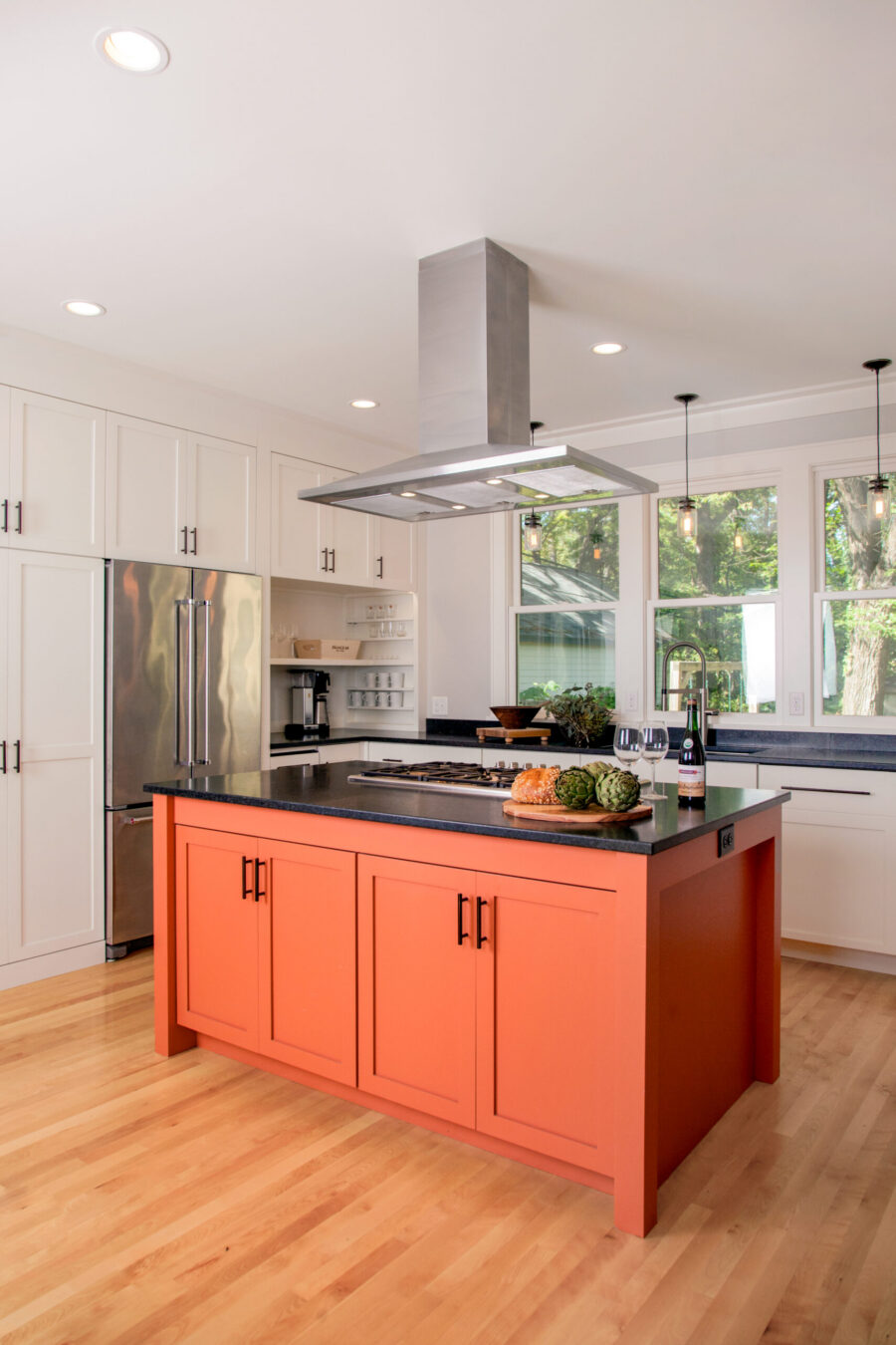 Renovated kitchen highlights vibrant orange island, white cabinetry, dark countertops.